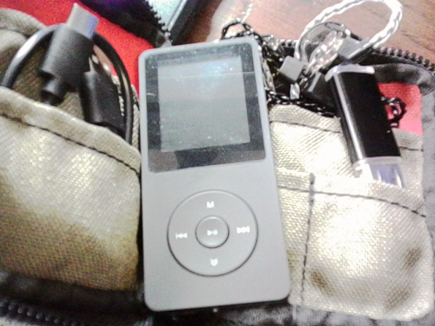 Black MP3 player with a small screen and scroll wheel style interface sitting on top of a small case containing a cable and headphones